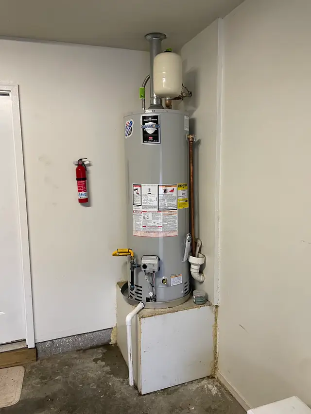 A new gas tank water heater with an expansion tank, set on a raised platform in a garage corner