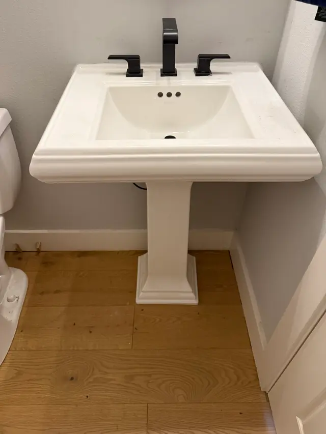 New pedestal sink with a matte black widespread faucet on a wood floor