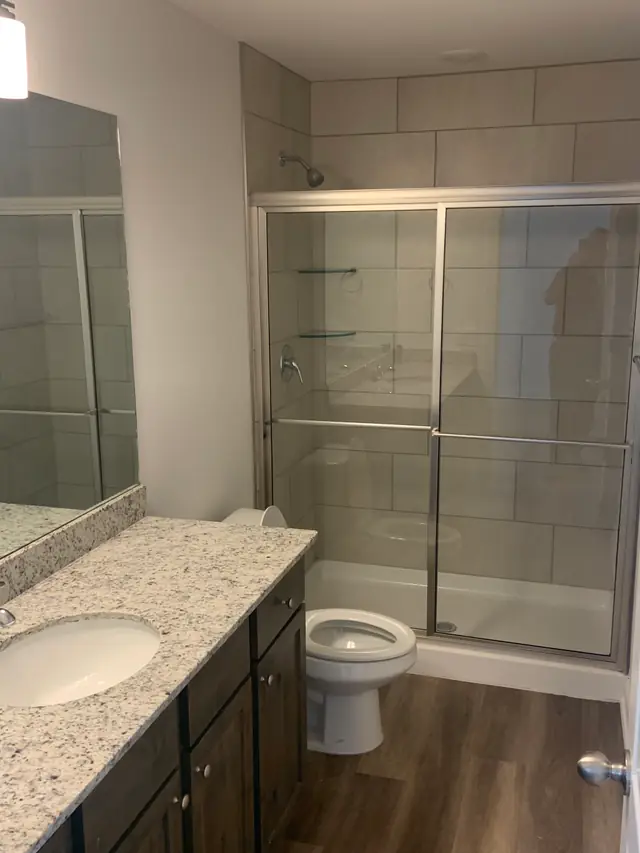 A finished bathroom with a granite vanity, a new toilet and a framed glass shower