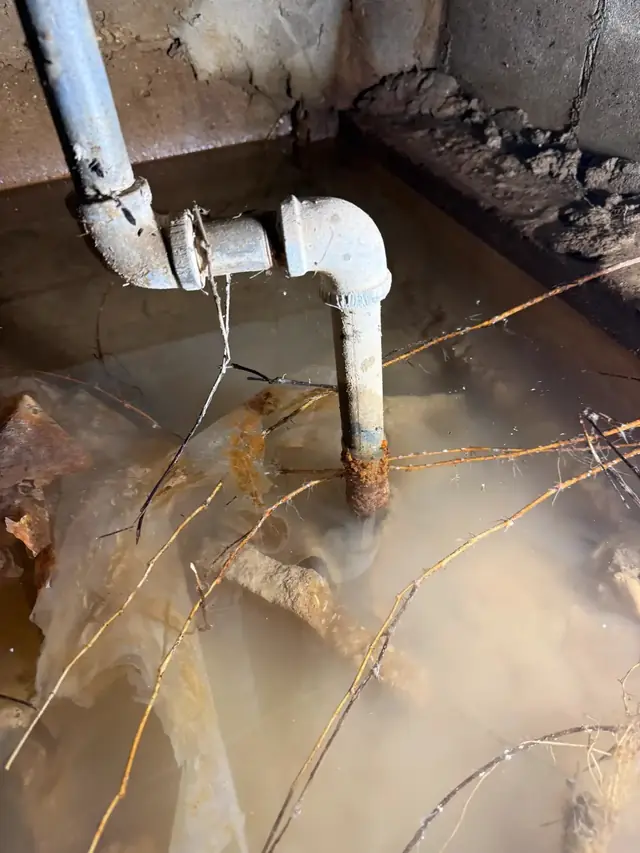 A corroded galvanized pipe standing over a flooded crawl space pit
